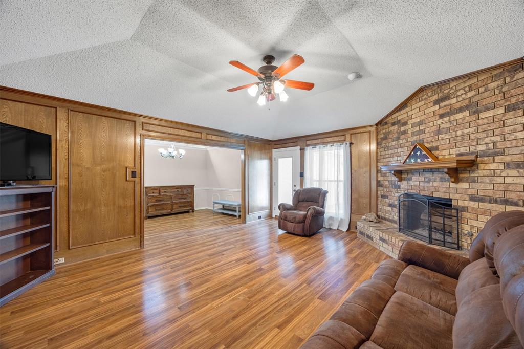 Vaulted ceiling, floor-to-ceiling wood paneling, wood-finish flooring, and a brick fireplace featuring a wood mantel