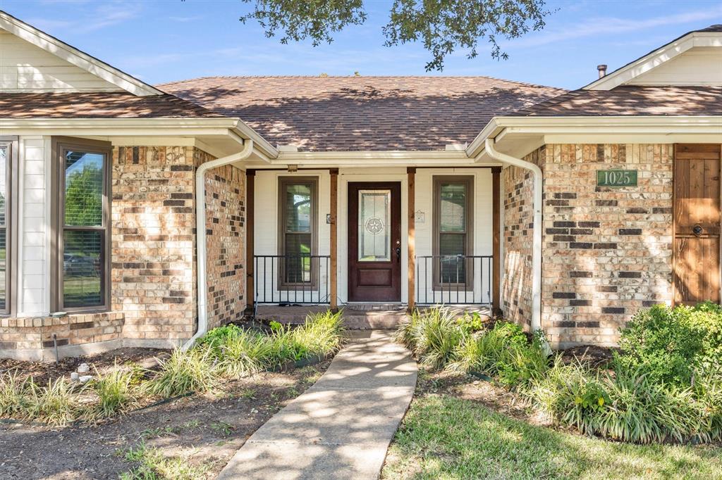 Brick exterior facade featuring a covered front porch, dark-stained wooden support posts, black metal railings, and a decorative glass-panel front door