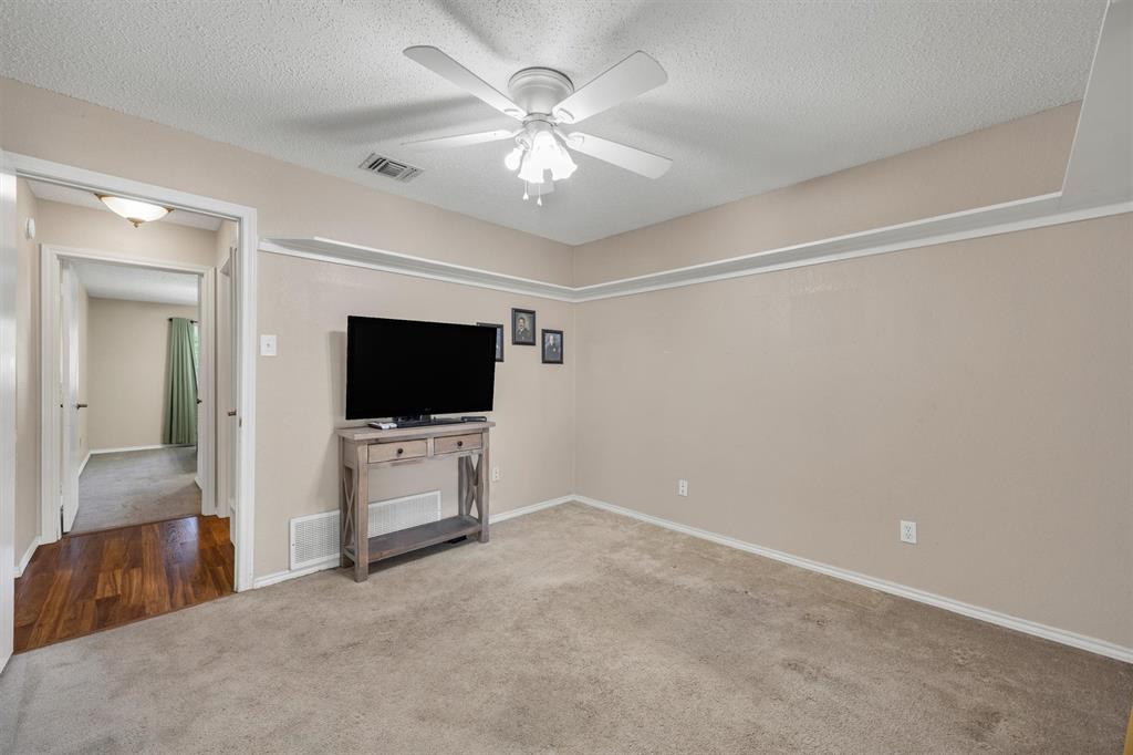 Neutral-toned interior featuring wall-mounted crown molding, ceiling-mounted light fixture with a fan, carpeting, and wood-finish flooring