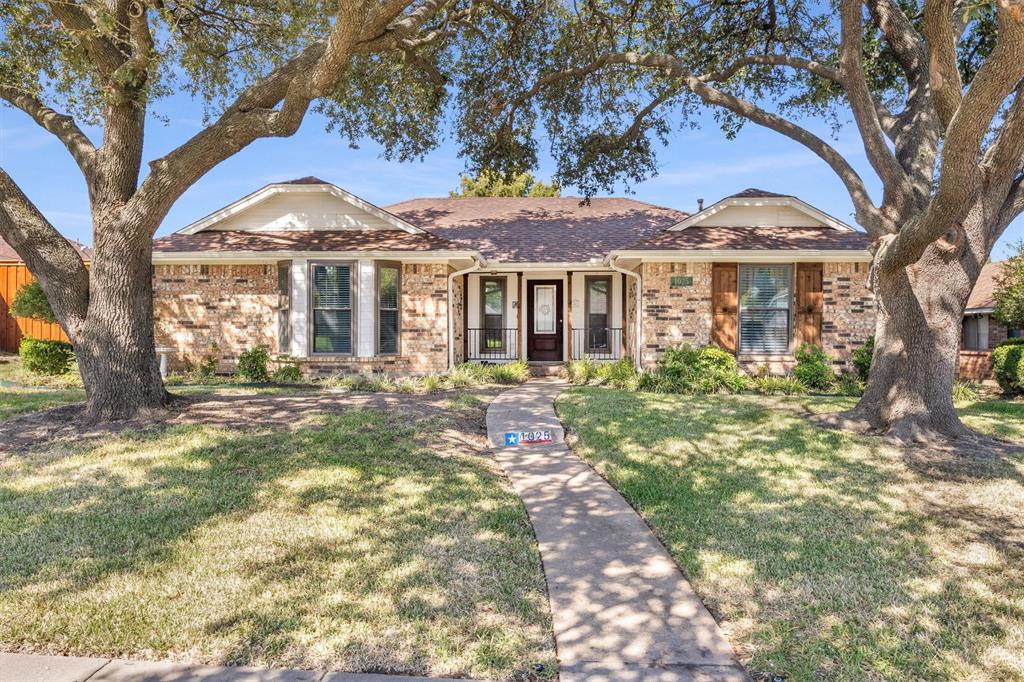 Single-story brick exterior featuring a multi-gabled roofline, front-facing bay windows, wood-shutter accents, and mature shade trees