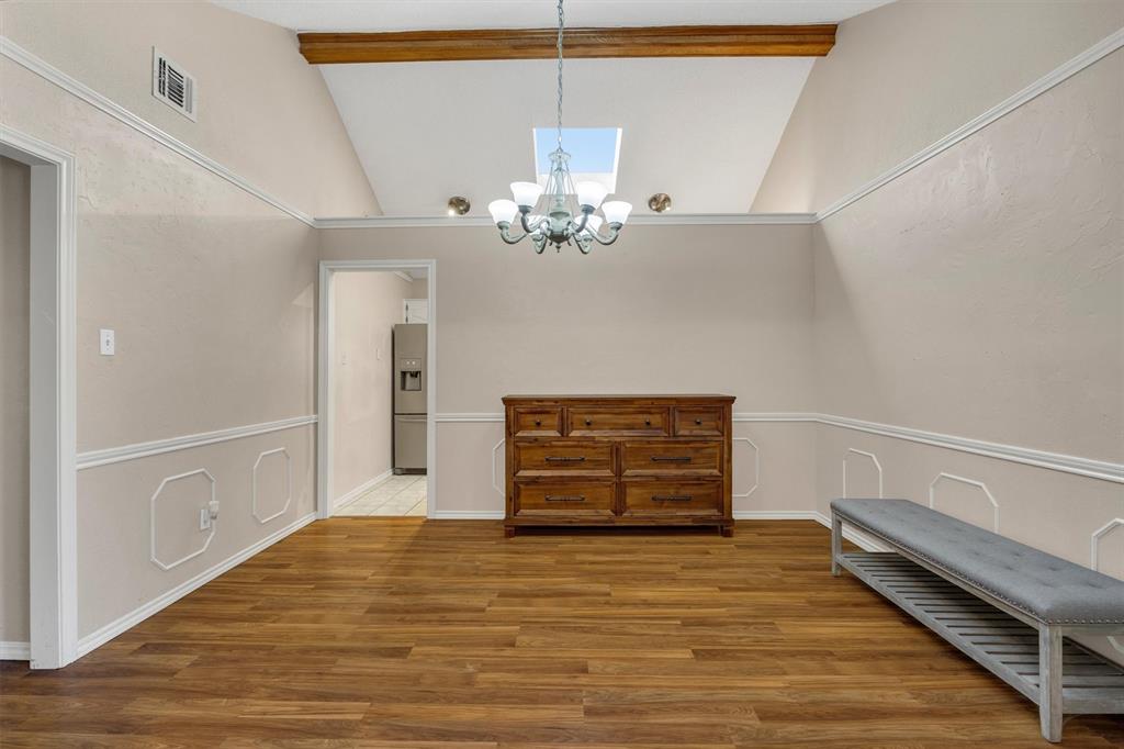 Vaulted ceiling featuring a central exposed wooden beam, skylight, and decorative crown molding, paired with wood-finish flooring and wainscoting