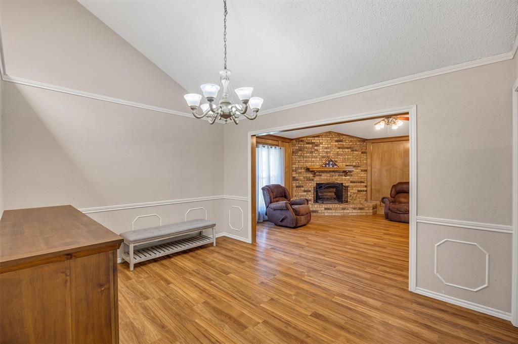 Vaulted ceiling with a multi-arm chandelier, wood-finish flooring, decorative wall molding, and a brick fireplace featuring a wood mantel