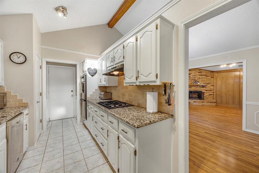 Kitchen featuring white cabinetry, stone-patterned countertops, tile flooring, built-in double wall ovens, and vaulted ceilings