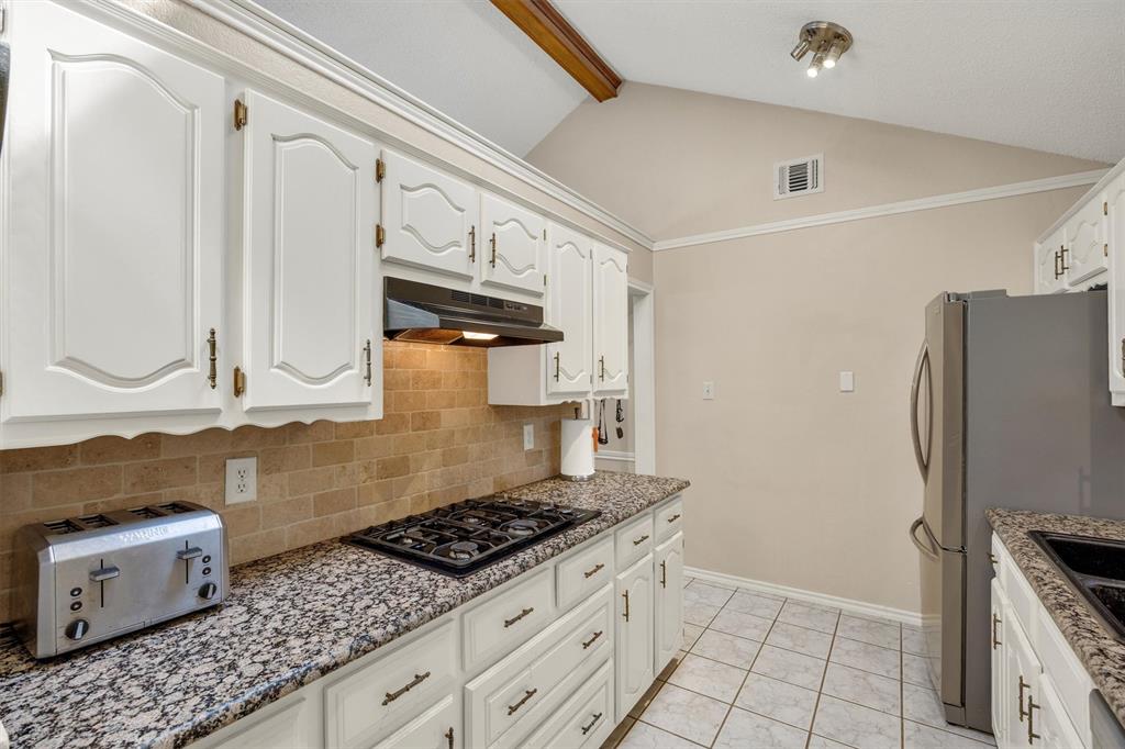 Kitchen featuring vaulted ceilings, white cabinetry with metallic hardware, stone-finish countertops, tiled backsplash, and stainless steel appliances