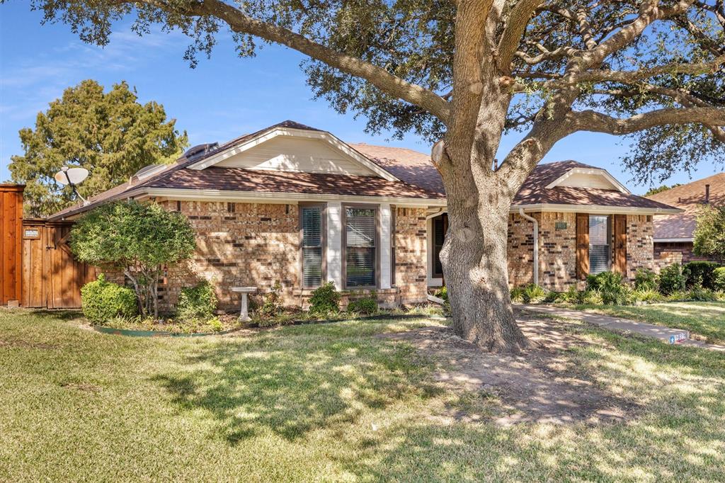 Single-story brick exterior featuring a hip roof, multi-pane windows, wood privacy fencing, and a mature tree