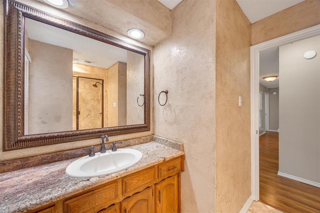 Vanity featuring a stone-surface countertop, integrated oval sink, and wood cabinetry, paired with a framed mirror, recessed lighting, and metallic wall-mounted hardware