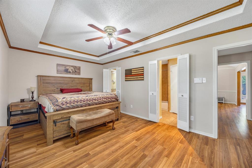 Tray ceiling with crown molding, wood-finish flooring, and integrated ceiling fan