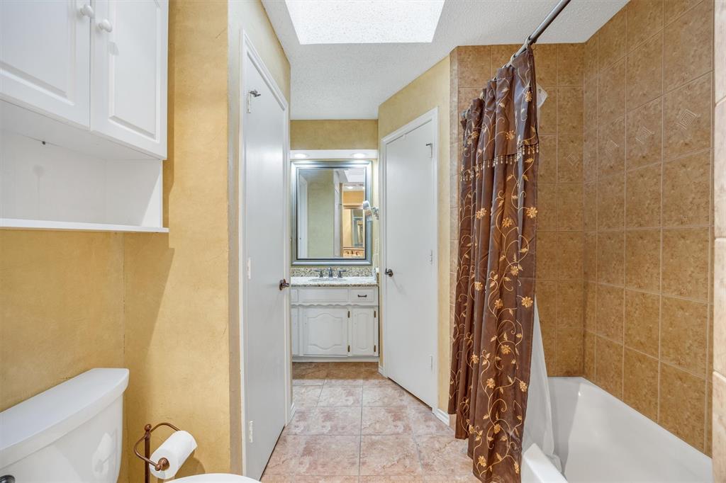 Bathroom featuring a skylight, tile flooring, vanity with stone-surface countertop, and a tiled shower surround