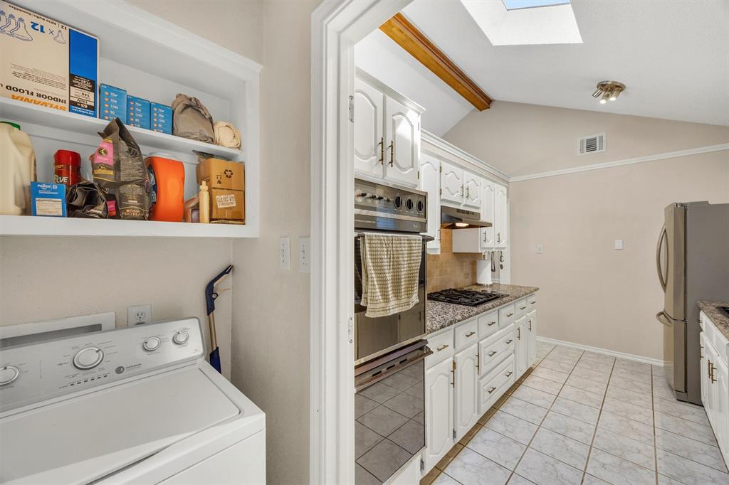 Kitchen featuring white cabinetry, stone-surface countertops, built-in dual wall ovens, and tile flooring, with a skylight and wood-beam ceiling detailing