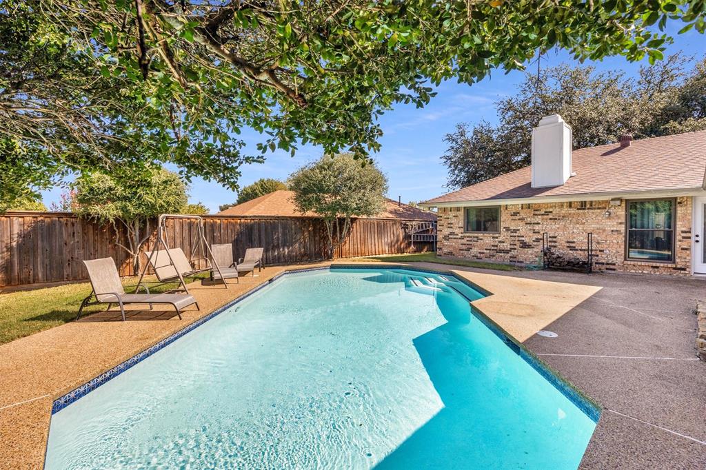 Backyard featuring an in-ground swimming pool, aggregate decking, brick exterior cladding, a masonry chimney, and perimeter wood fencing