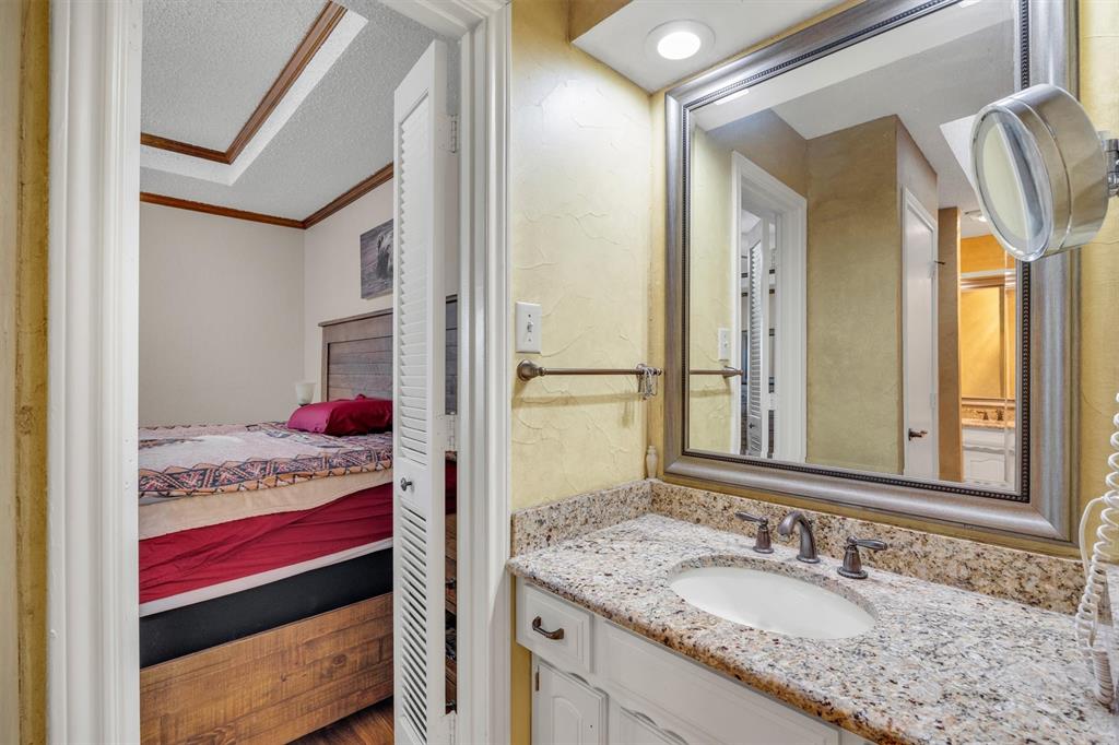 Bathroom vanity featuring a stone-composite countertop, undermount sink, multi-handle faucet, framed wall mirror, and white cabinetry