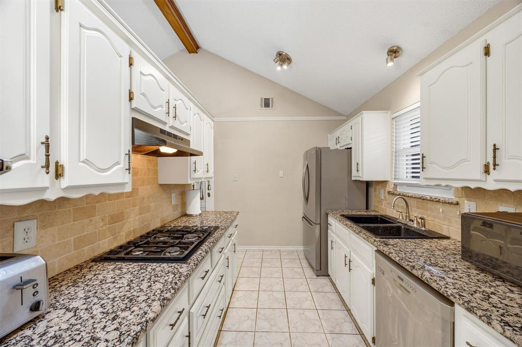 Kitchen featuring white cabinetry, stone-finish countertops, tile backsplash, stainless steel appliances, and vaulted ceilings