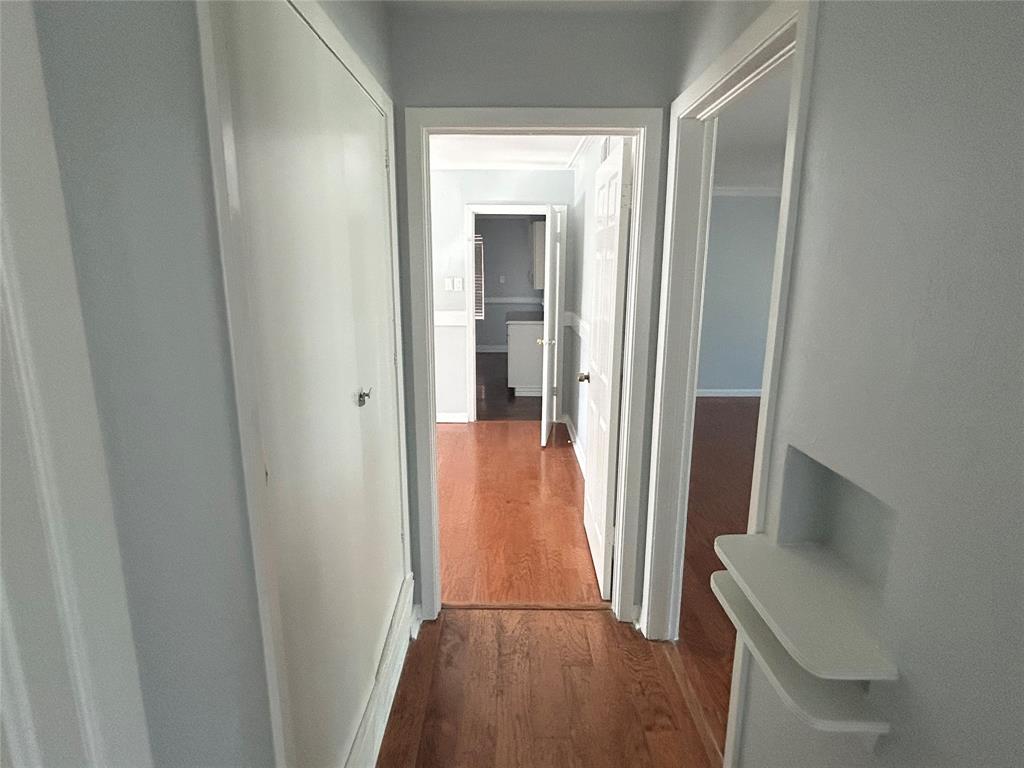 Hallway featuring wood-finish flooring, a built-in recessed wall niche with dual shelving, and flush-panel closet doors Hallway featuring wood-finish flooring, a built-in recessed wall niche with dual shelving, and flush-panel closet doors