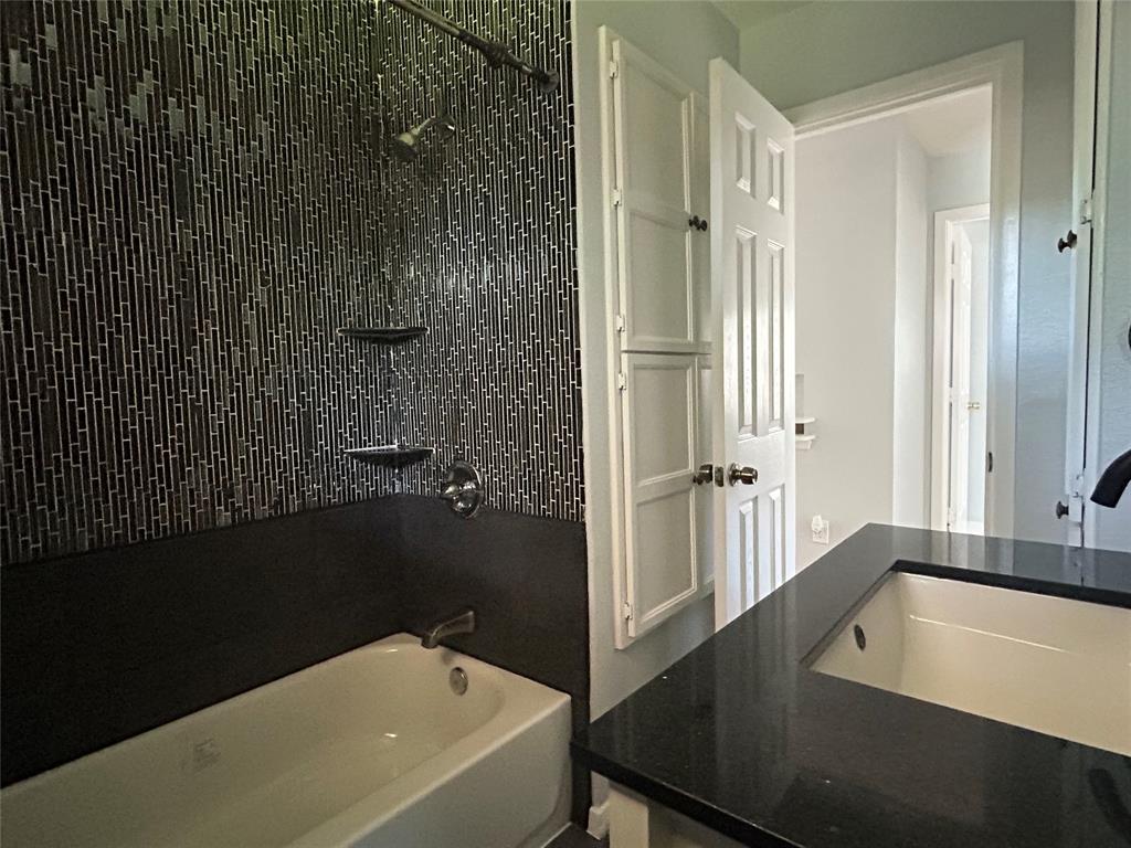 Bathroom featuring a deep-soaking tub, floor-to-ceiling vertical mosaic tile surround, built-in shelving, dark solid-surface countertop, and an integrated rectangular basin
