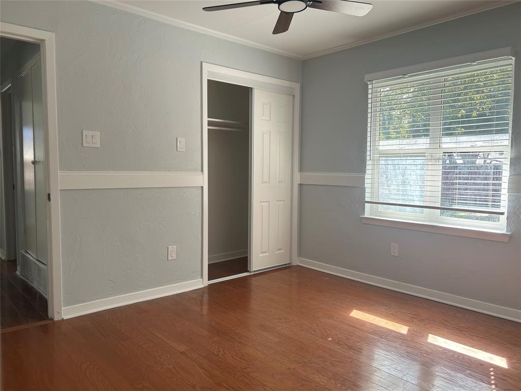 Room featuring wood-finish flooring, chair rail molding, ceiling fan, and sliding closet doors