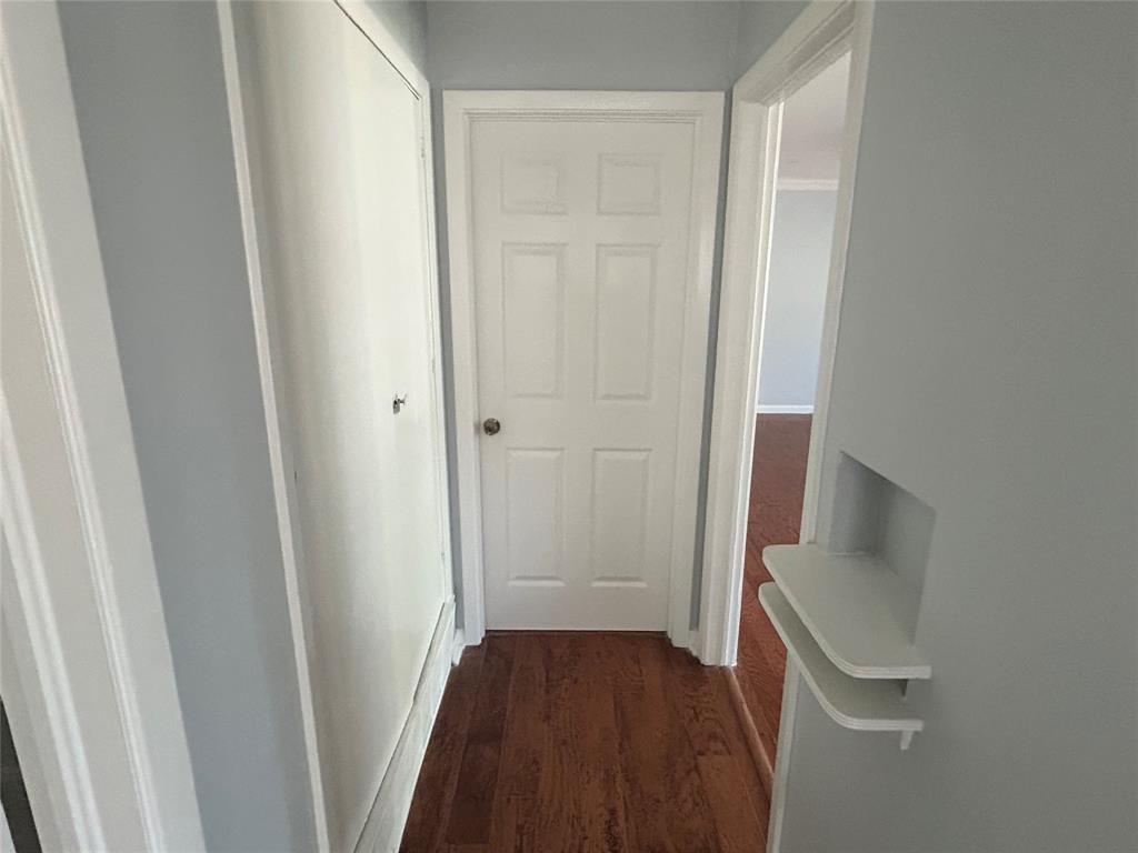 Hallway featuring wood-finish flooring, a six-panel door, floor-to-ceiling closet cabinetry, and a built-in recessed wall niche with dual shelving Hallway featuring wood-finish flooring, a six-panel door, floor-to-ceiling closet cabinetry, and a built-in recessed wall niche with dual shelving