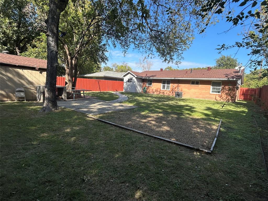 Fenced backyard featuring a brick exterior, stone patio, mature trees, and a ground-level gravel area