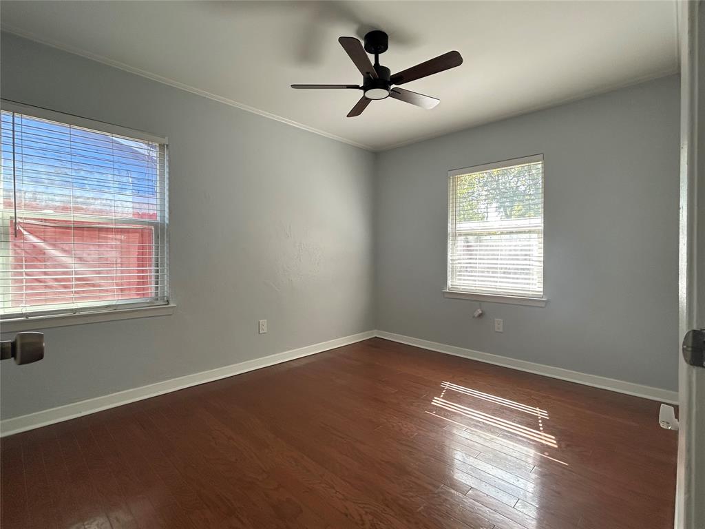 Room featuring wood-finish flooring, two windows with horizontal blinds, and a black ceiling fan with integrated lighting