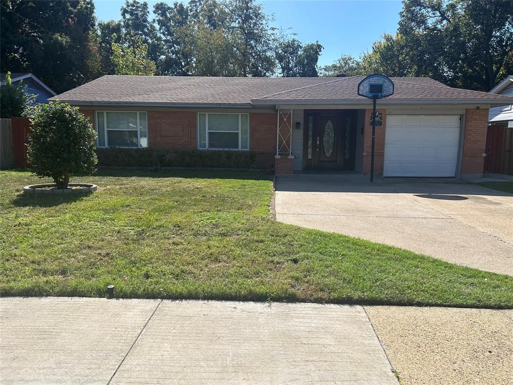 Single-story exterior featuring a brick facade, hipped roofline, concrete driveway, attached garage, and decorative front porch column