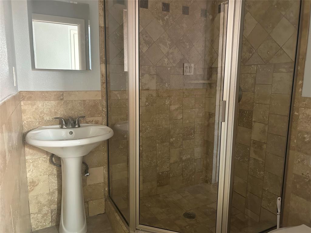 Pedestal sink with chrome faucet, corner shower enclosure featuring a metal frame, and natural stone tile wall surfacing