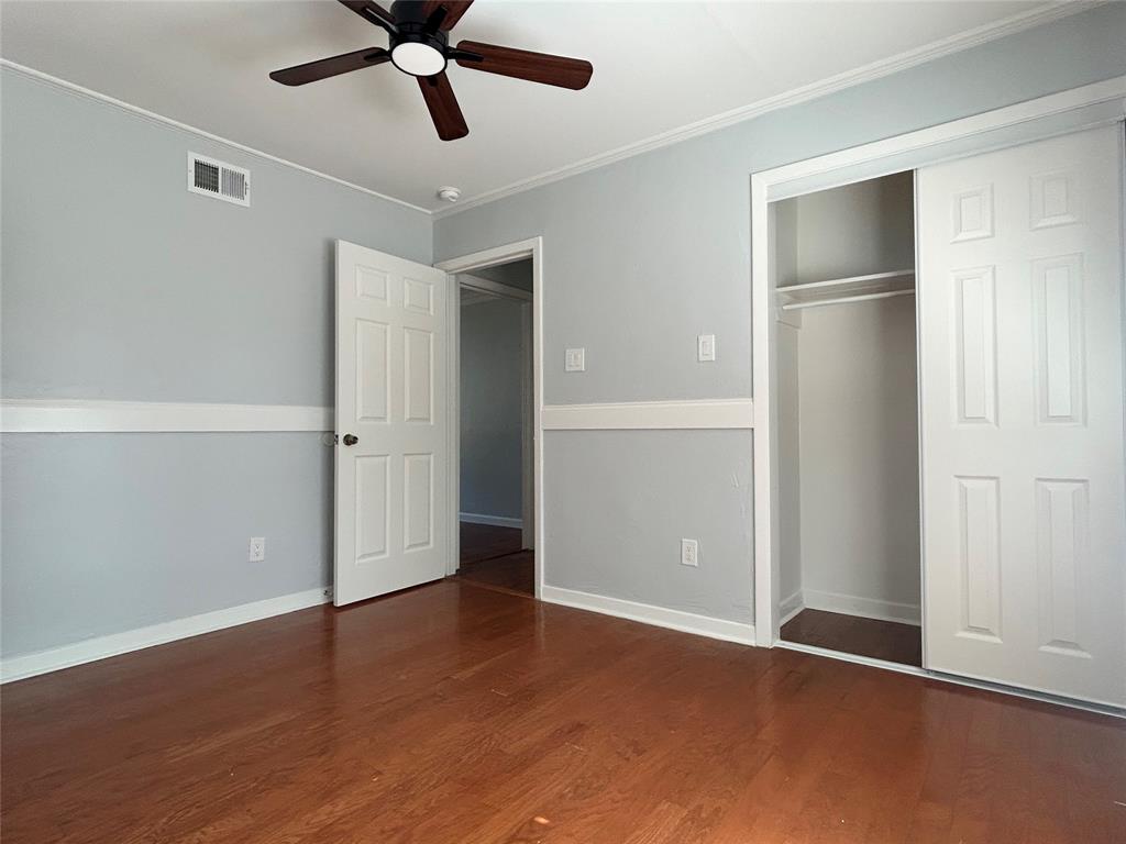 Wood-finish flooring, chair rail molding, ceiling fan with integrated lighting, and built-in closet with sliding doors
