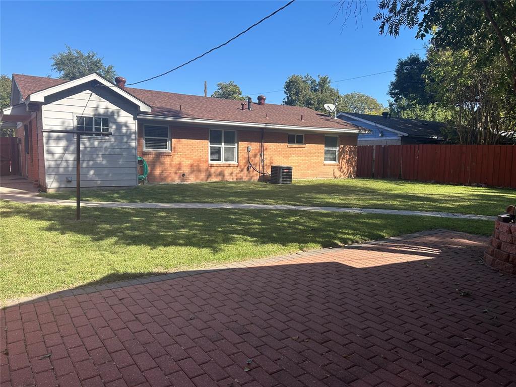 Backyard featuring a red brick paver patio, a grassy lawn, and red privacy fencing