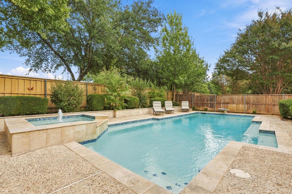 Backyard featuring an in-ground swimming pool, integrated spa with water feature, stone-finish decking, and wood privacy fencing