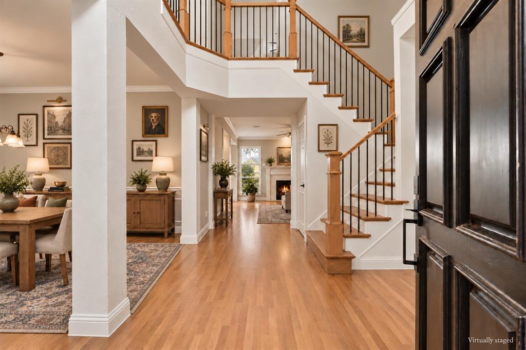 Foyer featuring wood-finish flooring, a staircase with a wooden handrail and metal balusters, and a fireplace with a decorative mantel
