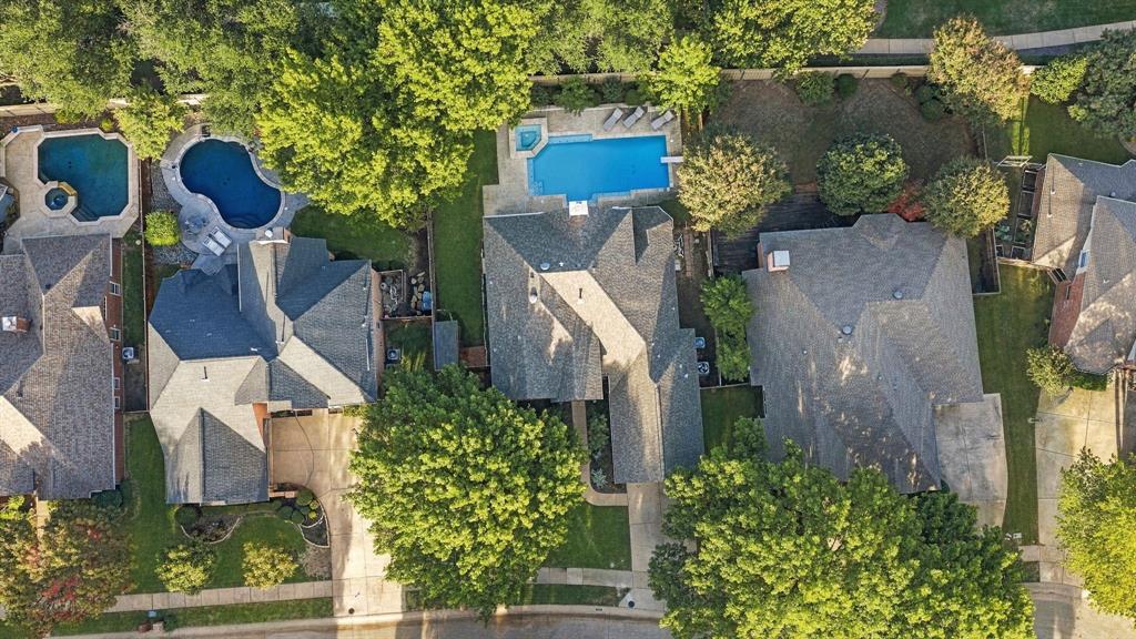 Aerial perspective showcasing a residential property featuring an in-ground swimming pool, an integrated spa, paved hardscaping, and mature trees on a landscaped lot