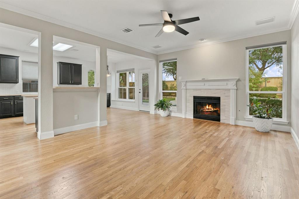 Living area featuring wood-finish flooring, a masonry fireplace with a white mantel, neutral wall tones, crown molding, and a ceiling fan with integrated lighting