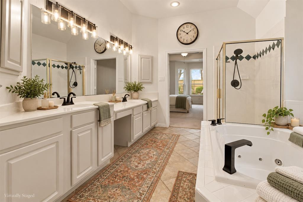 Dual-vanity cabinetry with solid-surface countertops, soaking jetted tub, enclosed glass-paneled shower with tiled inlay, and wall-mounted light fixtures