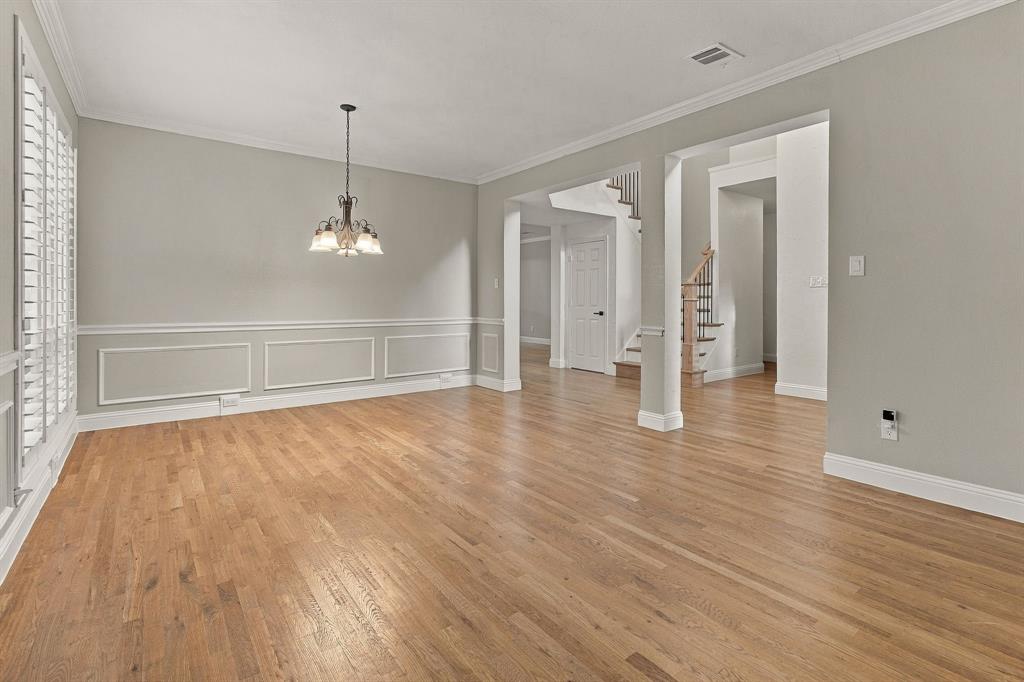 Interior room featuring wood-finish flooring, wainscoting, multi-pane window shutters, and a multi-arm chandelier