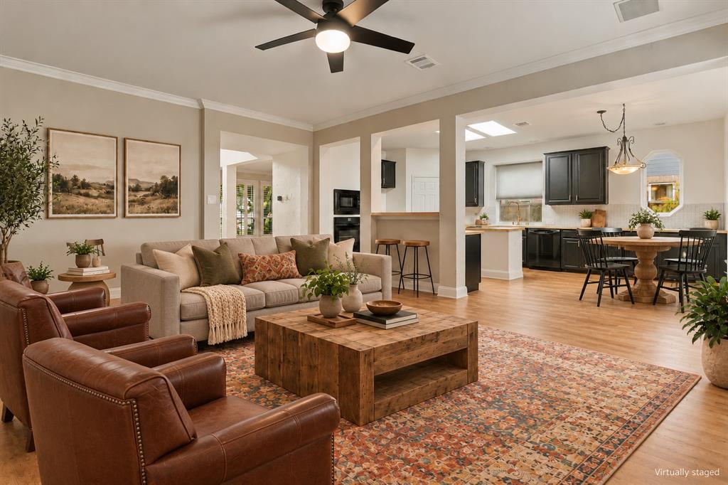 Open-concept interior featuring wood-finish flooring, recessed lighting, a modern ceiling fan, crown molding, and skylights