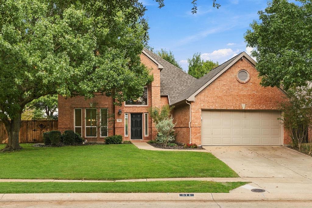 Two-story brick exterior featuring a multi-gabled roofline, an attached two-car garage, and mature landscaping
