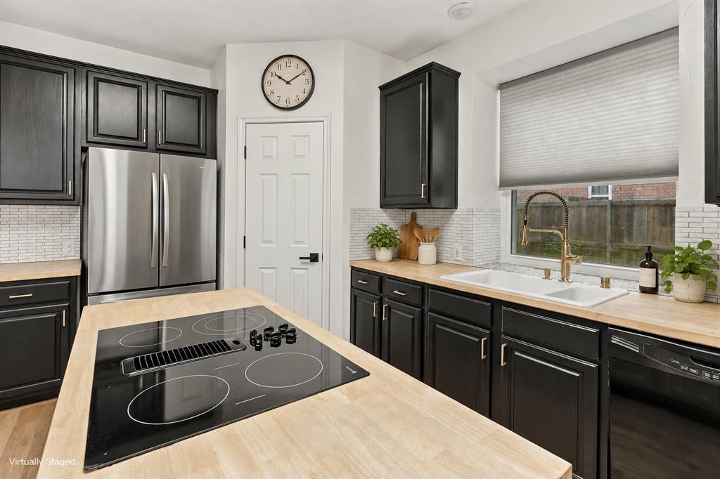 Kitchen featuring black cabinetry, wood-finish countertops, a central island with an integrated electric cooktop, stainless steel refrigerator, and white subway tile backsplash