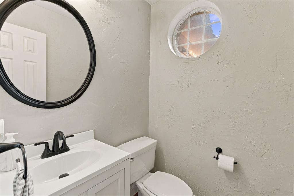 Bathroom featuring a white vanity cabinet, matte black faucet, circular black-framed mirror, and a decorative oval window with muntins