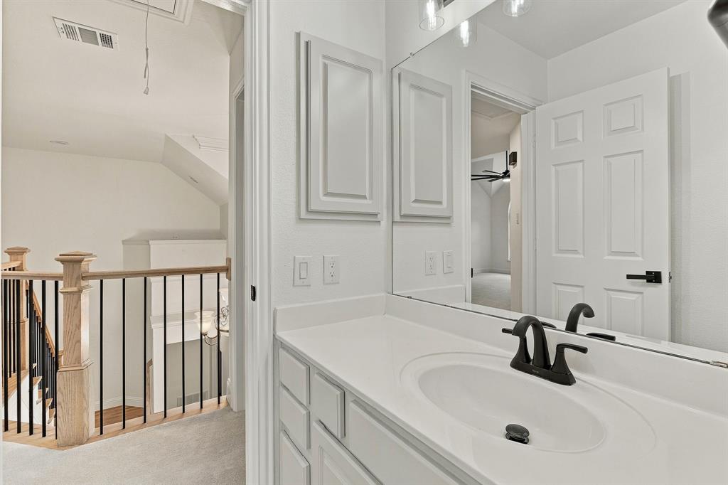 Vanity featuring a white countertop with an integrated oval basin and matte black faucet, full-width mirror, recessed cabinetry, and a staircase with a wooden banister and black metal balusters
