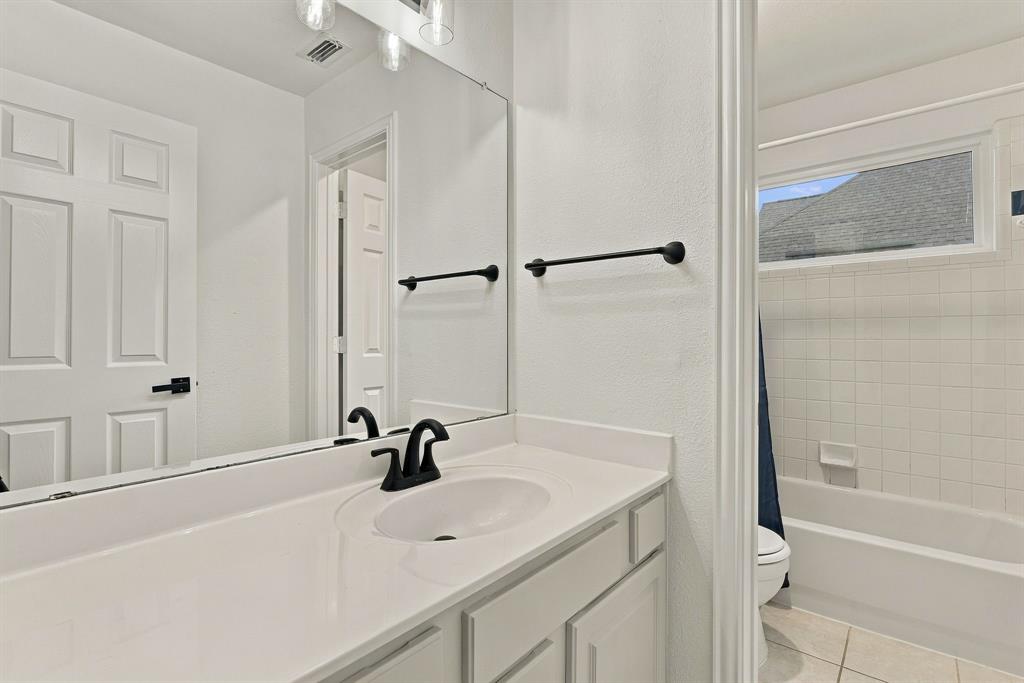 Bathroom vanity featuring a solid surface countertop, undermount sink, matte black faucet hardware, and a wall-to-wall mirror with multi-bulb overhead lighting