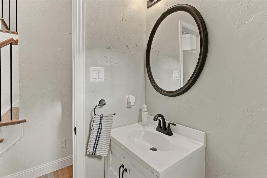 White vanity featuring a rectangular basin, matte black faucet, oval-framed mirror, and textured wall finish