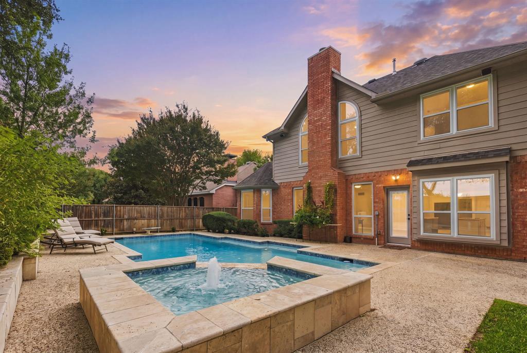Rear exterior featuring a brick and horizontal siding facade, a custom swimming pool with an integrated raised spa, a fountain feature, and a textured concrete patio