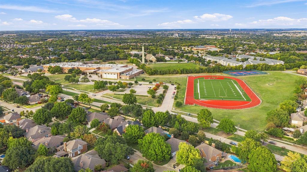 Aerial perspective of a residential neighborhood featuring established tree canopy, paved thoroughfares, athletic field with running track, and hardscaped courts
