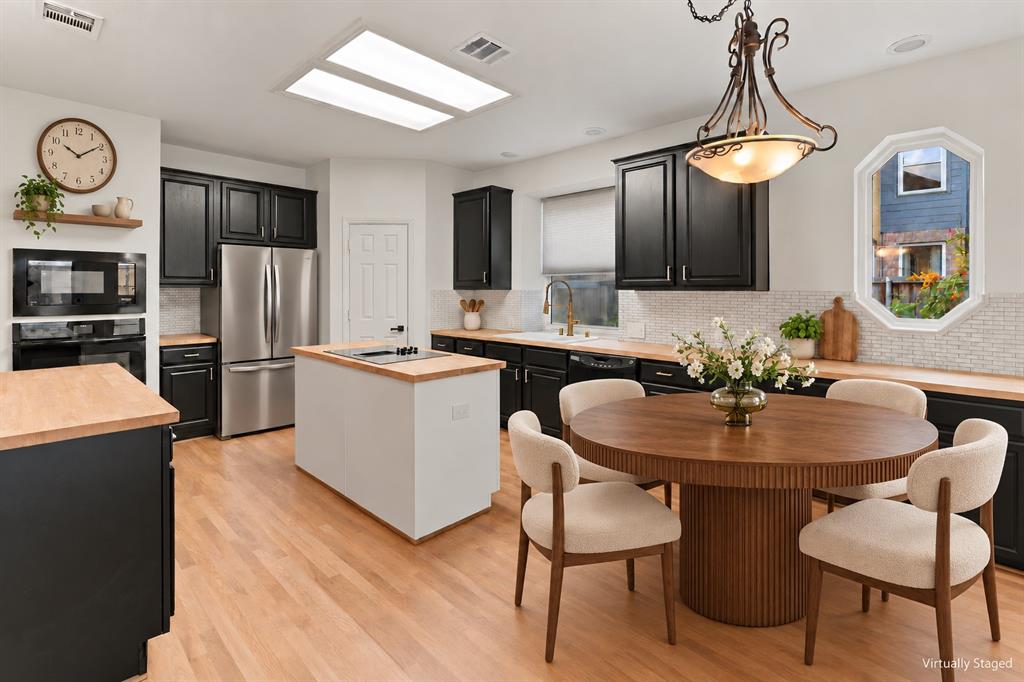 Kitchen featuring black cabinetry, wood-finish countertops, an island with a built-in cooktop, a mosaic tile backsplash, and recessed skylights