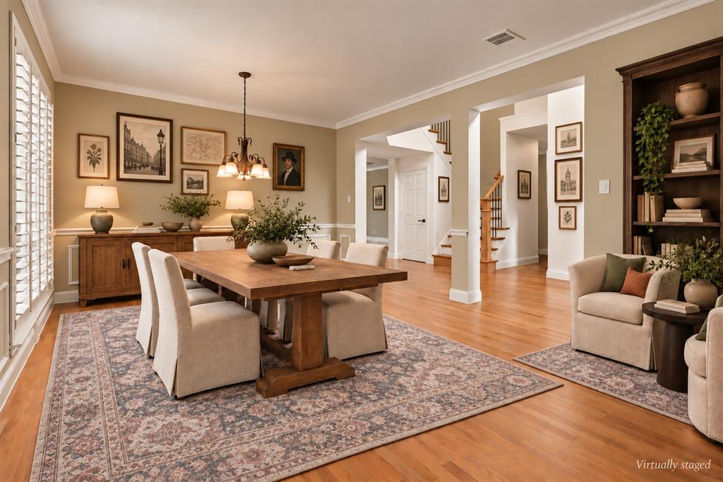 Dining area featuring wood-finish flooring, crown molding, plantation shutters, a tiered chandelier, and a built-in dark wood bookcase