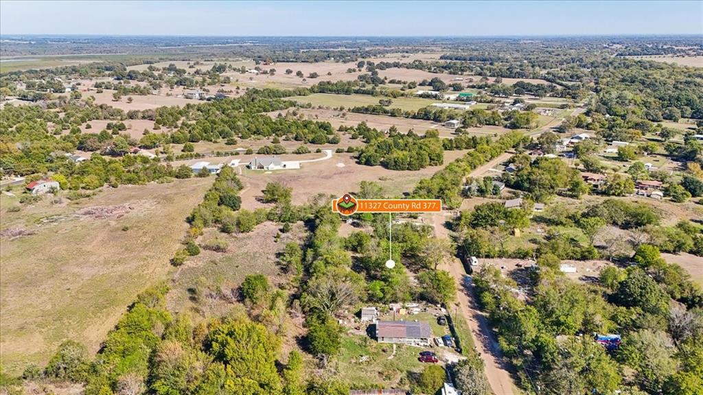 Aerial view of expansive rural acreage featuring mature trees, open pasture, and a paved road frontage Aerial view of expansive rural acreage featuring mature trees, open pasture, and a paved road frontage