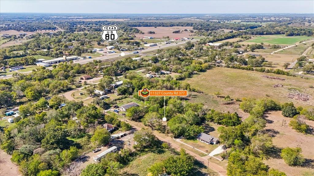 Aerial perspective of expansive acreage featuring mature trees, open pastureland, and a single-story structure with a paved driveway Aerial perspective of expansive acreage featuring mature trees, open pastureland, and a single-story structure with a paved driveway