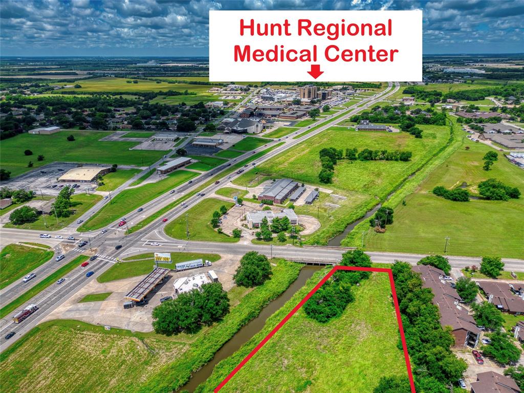 Aerial perspective of vacant land featuring defined boundaries, proximity to arterial roads, and established perimeter vegetation
