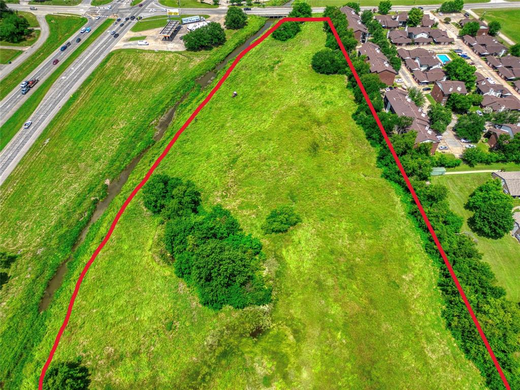 Expansive undeveloped parcel featuring open grassy terrain, clusters of mature trees, and a bordering natural drainage way