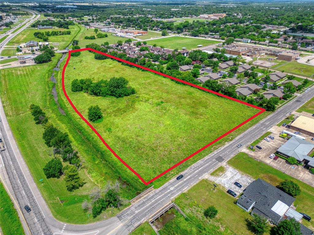 Expansive parcel of land featuring open green space, mature trees, and frontage along a paved thoroughfare