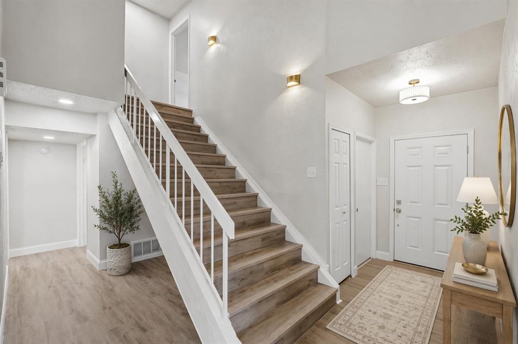 Entryway featuring wood-finish flooring, a staircase with white metal railings, recessed ceiling lighting, wall-mounted metallic sconces, and a panelled front door
