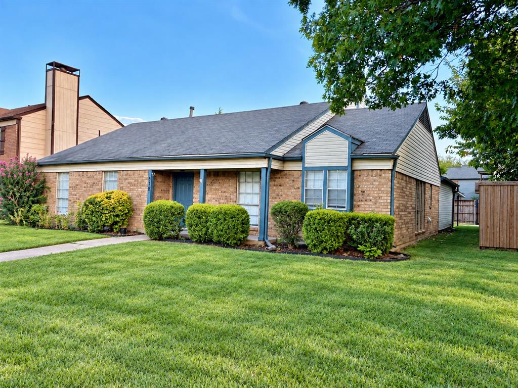 Single-story brick exterior featuring a multi-gabled roofline, covered front entryway, paneled siding accents, and a front lawn with established landscaping